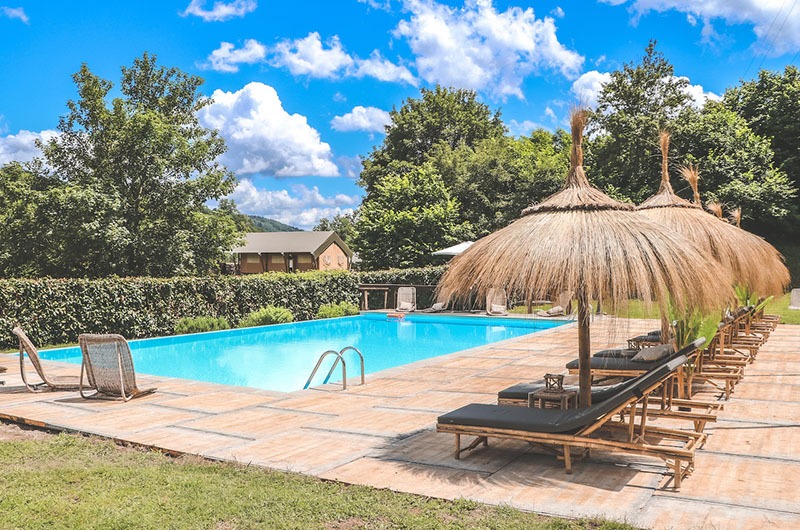 Pool des Agriturismo Rancone Lodges mit Liegen und Sonnenschirmen in ländlicher Umgebung