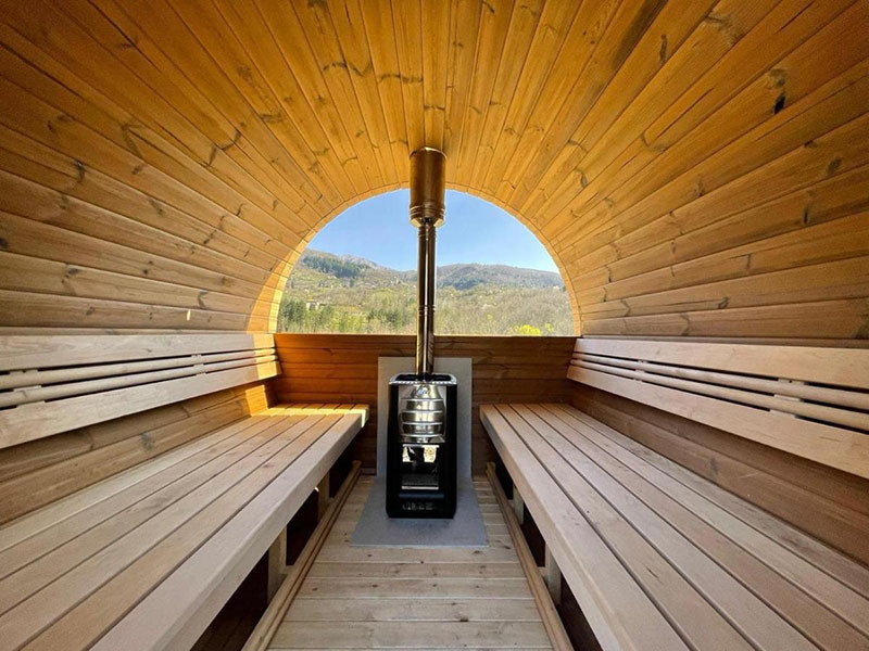 Innenansicht einer Holzsauna im Agriturismo Rancone Lodges bei Lucca mit Panoramafenster und Blick auf die toskanischen Berge.