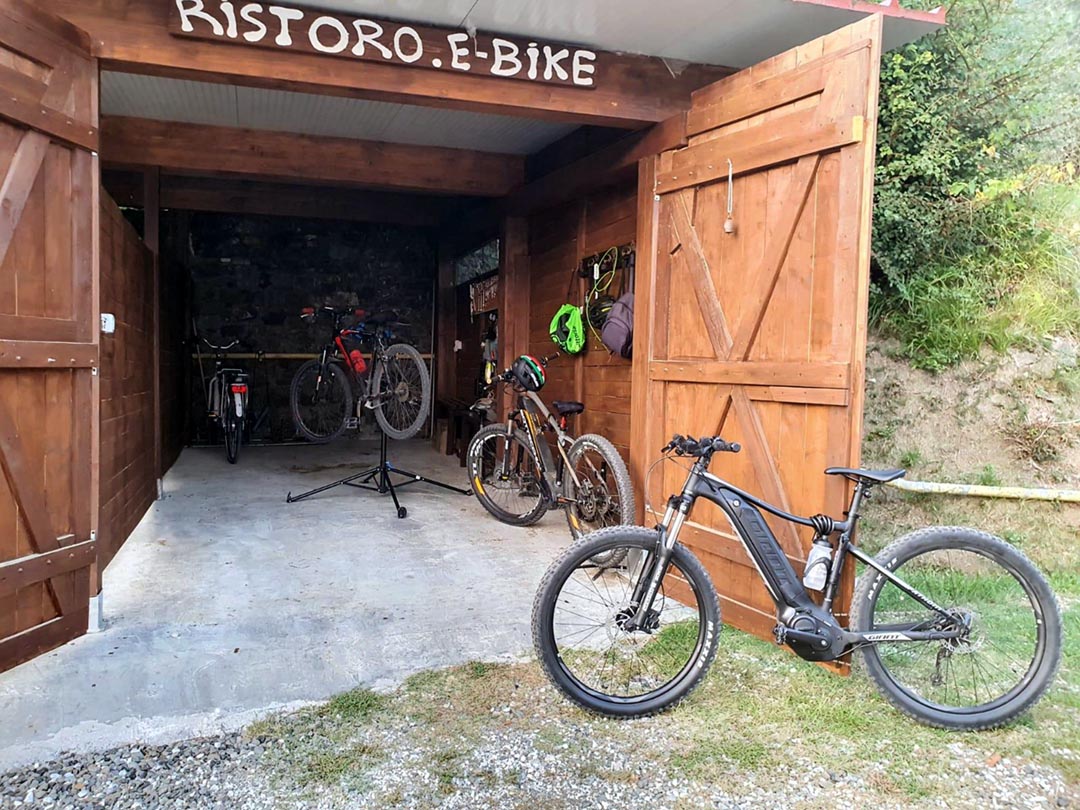 Holzgarage des Agriturismo La Bianca Fattoria mit E-Bikes und Fahrrädern, ausgestattet mit Werkbank, Reparaturständer und Ladestationen für Gäste.