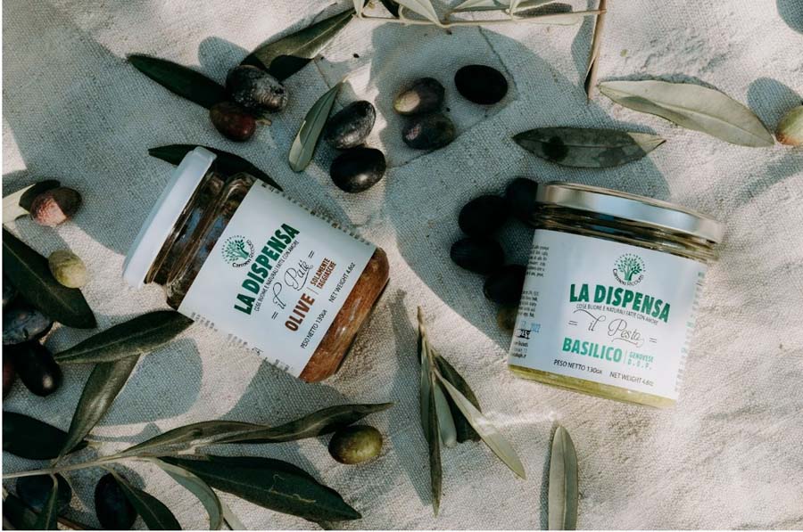 Gläser mit Olivenpaté und Basilikumpesto aus der Produktion des Agriturismo Cà di Ughi, dekoriert mit frischen Oliven und Zweigen auf hellem Tuch.