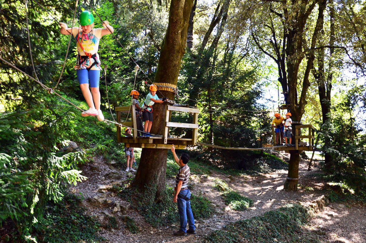 Kinder auf einer Seilbrücke zwischen Bäumen im ligurischen Abenteuerpark Val di Vara