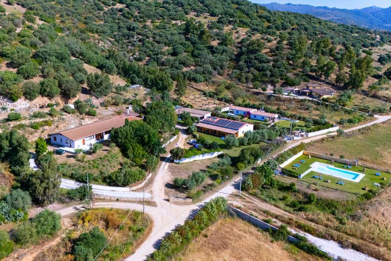 Luftaufnahme eines Agriturismo mit mehreren Gebäuden, Zufahrtswegen, Pool und grüner Gartenfläche in hügeliger Landschaft.