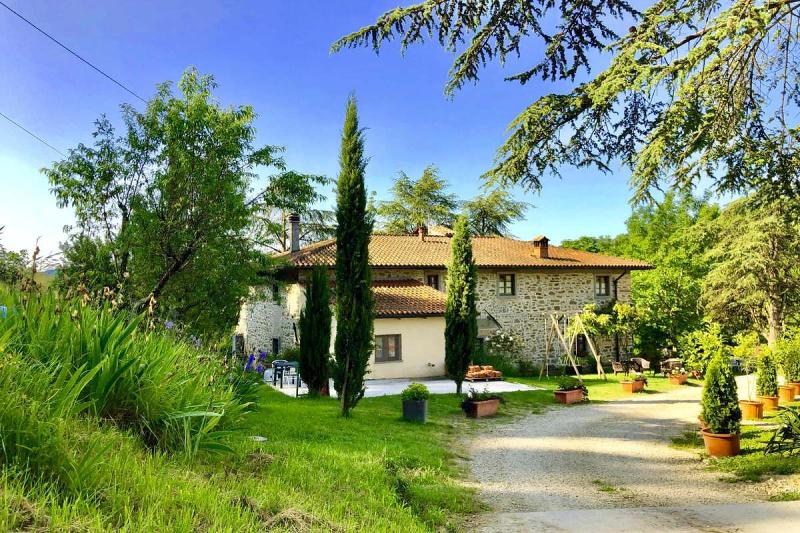 Das Agriturismo Podere Badia ValDrago in der Toskana: ein restauriertes Steinhaus mit Terrakotta-Dach, umgeben von Zypressen, blühenden Pflanzen und viel Grün. Der Hof liegt idyllisch eingebettet in eine sonnige, naturnahe Landschaft.