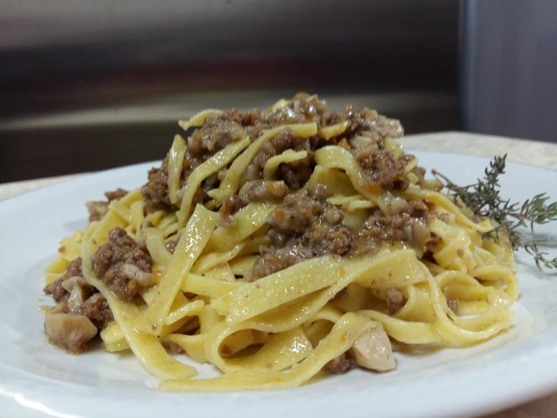 Ein Teller frische, handgemachte Tagliatelle mit würziger Fleischsauce, liebevoll zubereitet von Lucia auf dem Agriturismo Val di Boccio in Umbrien. Die goldgelbe Pasta wird appetitlich angerichtet und mit einem Zweig frischer Kräuter garniert.
